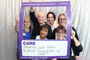 Six women stand inside a frame that reads 'South Metropolitan health Service: Care'. A handwritten message on the board reads 'Supporting our staff to provide excellence in care.'