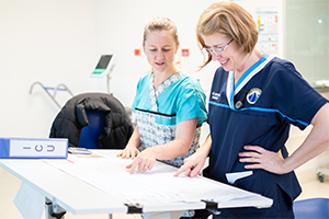 Two female nurses review paperwork at a standing desk