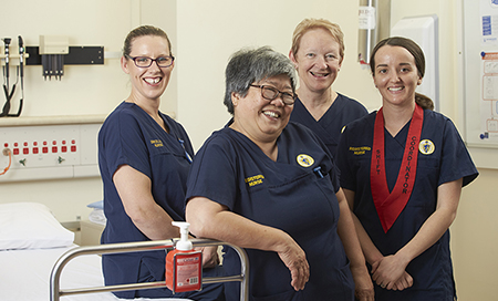 Four female nurses in Fremantle Hospital uniforms standing next to a hospital bed. 