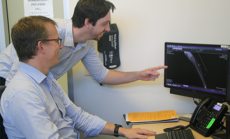 Two men review an x-ray image on a computer screen